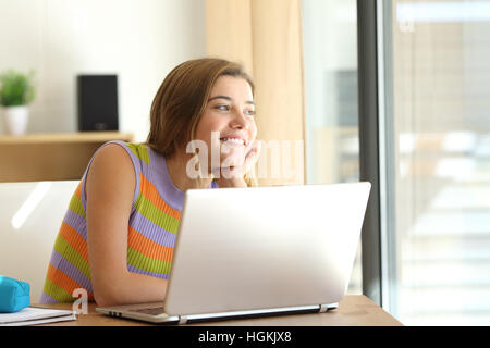 Ritratto di uno studente adolescente di pensare e di guardare fuori attraverso una finestra in un computer desktop a casa con una luce calda Foto Stock