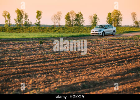 Gomel, Bielorussia - Maggio 04, 2016: Volkswagen Polo berlina auto parcheggio sul campo di grano. Sunset Sunrise colore giallo Sky su uno sfondo nella soleggiata sera. Foto Stock