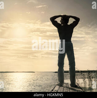 Silhouette di un uomo in piedi sul piccolo pontile in legno ad estate giornata di sole Foto Stock
