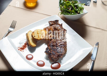 Bistecca con patate alla griglia con insalata lato su una piastra bianca Foto Stock