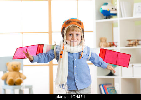Ragazzo bambino vestito come un pilota con ali giocattolo giocare in casa Foto Stock
