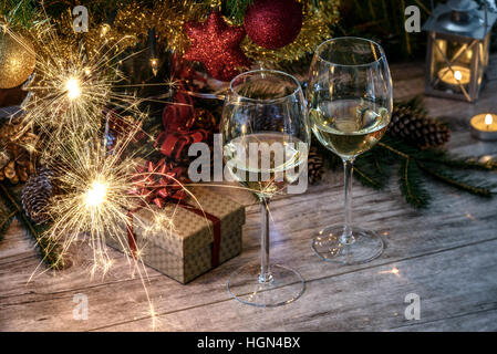 Botti a due wineglas con vino bianco su una tavola di legno in background di albero di Natale, dono e candele Foto Stock