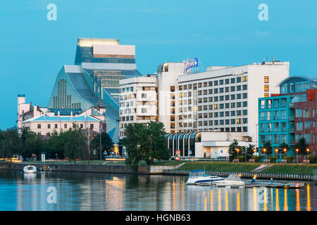 Riga, Lettonia - 30 Giugno 2016: la sera Cityscape presso la banca di fiume Daugava. Vista urbano di edificio della Biblioteca Nazionale serratura della luce e Contempora Foto Stock