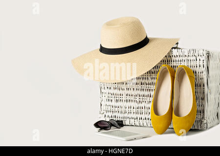 Bianco vimini valigia, womens cappello, occhiali da sole, scarpe di colore giallo e e-book. Foto Stock