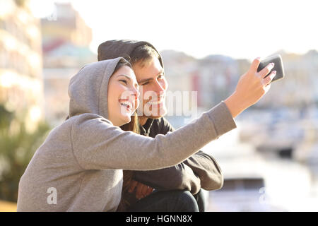 Coppia di ragazzi prendendo un selfie con uno smart phone all'aperto nei giorni festivi con una porta in background Foto Stock