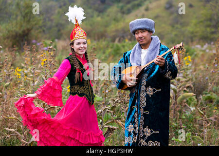 Uomo kazako che suona lo strumento musicale nazionale della dombra e della donna in balli rossi ad Almaty, Kazakistan Foto Stock