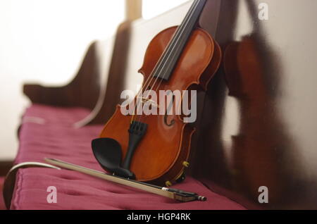 Il violino con inclinazione di prua e riflettendo su schienale in legno di borgogna o rosso scuro chiesa pew Foto Stock