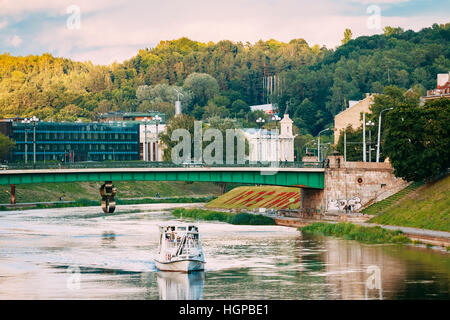 Vilnius Lituania - Luglio 08, 2016: il bianco imbarcazioni da diporto con passeggeri a bordo di flottazione sul fiume Neris sotto il ponte verde nella zona della città in Evenin Foto Stock