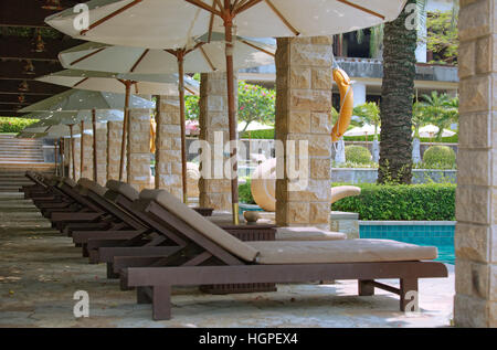 Fila di sedie a sdraio e ombrelloni da sole si trova in prossimità di una piscina dell'hotel Foto Stock