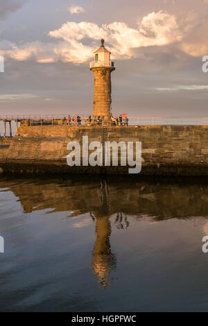 Oriente Pier lighthouse, porto di entrata e di persone, illuminato dal sole di sera e riflessa nel mare - Whitby, North Yorkshire, GB. Foto Stock