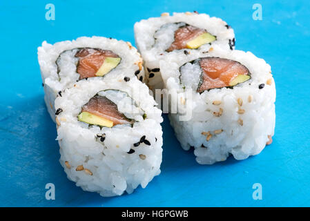 Quattro preparata di fresco salmone crudo e avocado urumaki sushi rotoli in una vista ravvicinata su uno sfondo blu concettuale del giapponese cucina a base di pesce Foto Stock