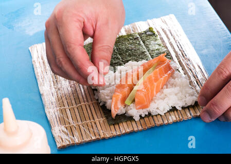 Close up di chef le mani sul tappetino con piatti a base di pesce e per il riso facendo Temaki sushi roll Foto Stock