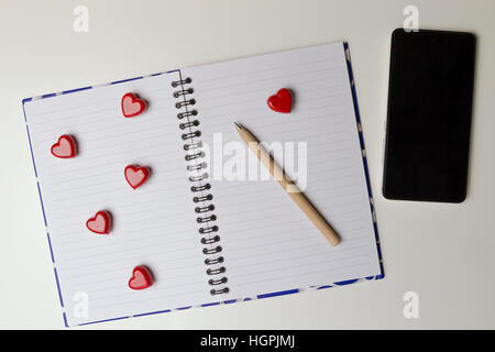 Aprire il notebook con cuore rosso e il telefono cellulare su sfondo bianco. Vista superiore Foto Stock