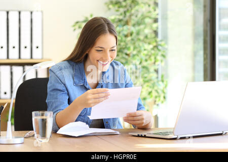 Felice imprenditore donna lettura buona notizia in una lettera a una scrivania in ufficio Foto Stock