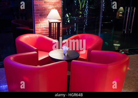 Divano rosso intorno al piccolo tavolo in discoteca illuminazione dal lampada, nessun popolo Foto Stock