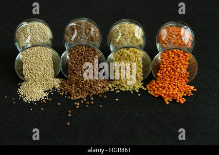 Quattro differenti: semole e semolini di grano saraceno, lenticchia, quinoa, bulgur, in vetri trasparenti su sfondo nero Foto Stock