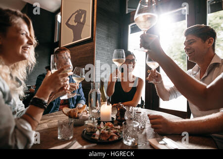Gruppo di amici fare un brindisi al ristorante. Giovani amici seduti ad un tavolo, di tostatura con vino e godersi un pasto serale insieme.