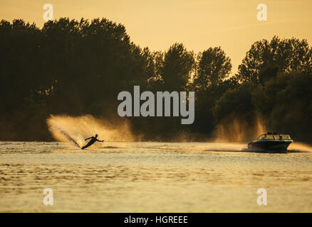 L'uomo Wakeboard sul lago dietro la barca al tramonto. Sci d'acqua sul lago. Foto Stock