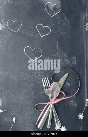 Vista superiore del giorno di San Valentino la cena messa in tavola con posate su una lavagna rustico sfondo con le luci fairy e Instagram tipo filtro sbiadito. Foto Stock