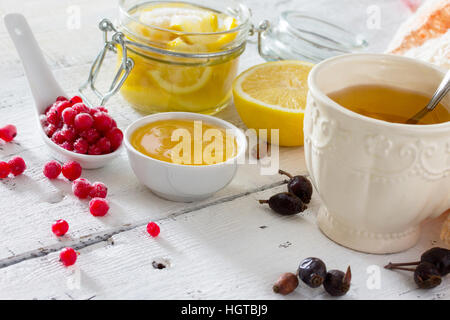 Il trattamento di raffreddori stagionali - trattamento nella medicina popolare, fonti dietetiche di vitamina su un tavolo bianco: Limone, miele, rosa canina, bacche, ribes rosso. Foto Stock