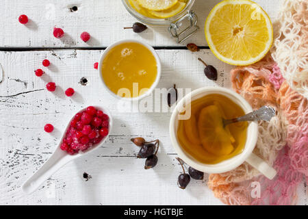 Il trattamento di raffreddori stagionali - trattamento nella medicina popolare, fonti dietetiche di vitamina su un tavolo bianco: Limone, miele, rosa canina, bacche, ribes rosso. Foto Stock