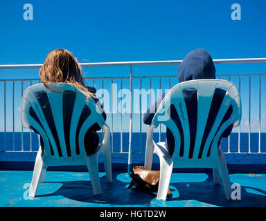Due passeggeri seduti in sedie di plastica sul ponte di una nave passeggeri che guarda al mare su una tranquilla giornata estiva con cielo blu Foto Stock