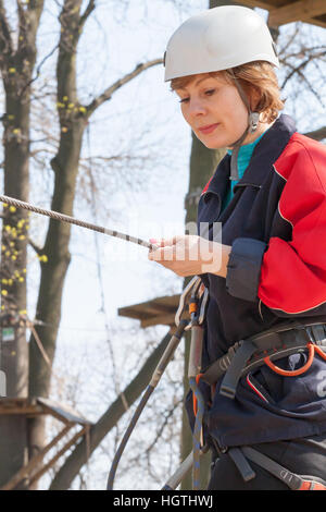 La ragazza si arrampica ostacoli del parco di corda in chiaro giorno di estate Foto Stock