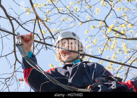 La ragazza si arrampica ostacoli del parco di corda in chiaro giorno di estate Foto Stock