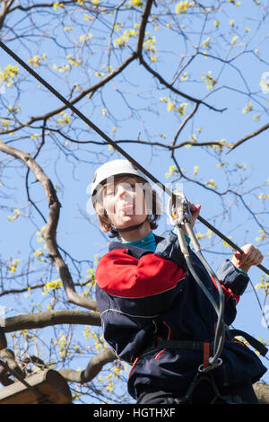 La ragazza si arrampica ostacoli del parco di corda in chiaro giorno di estate Foto Stock