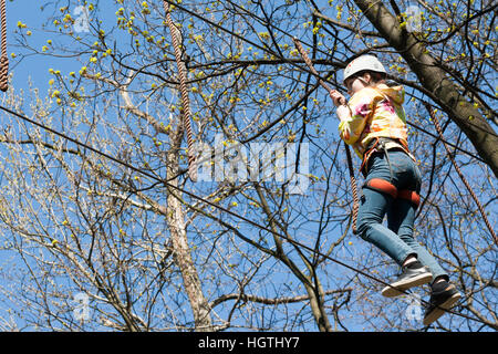 La ragazza si arrampica ostacoli del parco di corda in chiaro giorno di estate Foto Stock