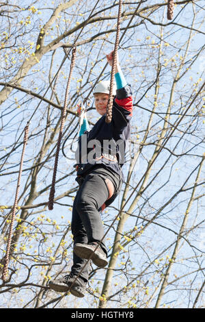 La ragazza si arrampica ostacoli del parco di corda in chiaro giorno di estate Foto Stock