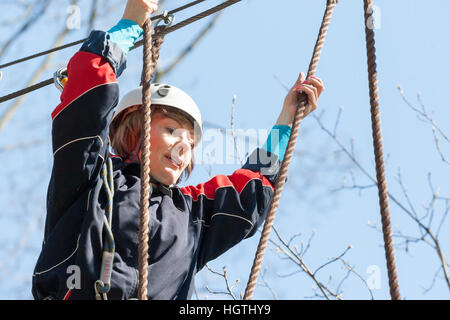 La ragazza si arrampica ostacoli del parco di corda in chiaro giorno di estate Foto Stock