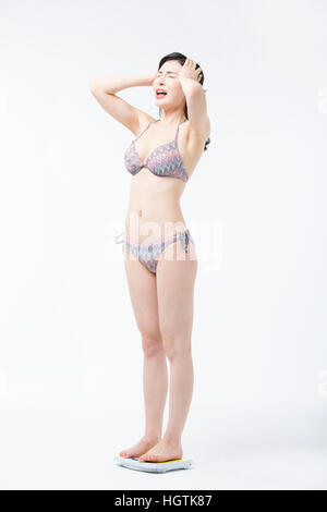 Vista laterale della giovane donna stressante in bikini in piedi su una scala Foto Stock