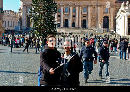 Due amici prendendo saelfie utilizza lo smartphone con il bastone a Piazza San Pietro (Piazza San Pietro) Città del Vaticano, in inverno una giornata di sole. Il Natale di Roma Foto Stock