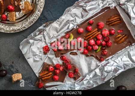 Barra di cioccolato con frutti di bosco e i dadi in lamina su sfondo scuro Foto Stock
