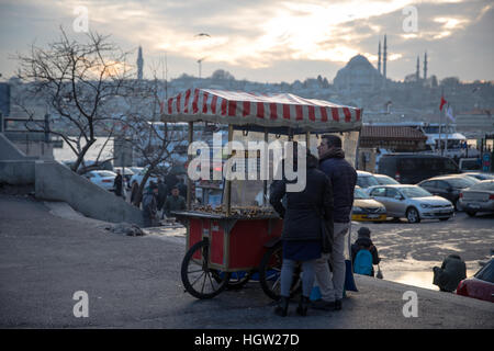 Un paio di acquistare mais dolce caldo da un venditore ambulante di Istanbul con uno della città molte moschee visibile in background. Foto Stock