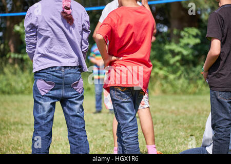 Un gruppo di ragazzi in jeans in piedi su un campo in erba con le spalle alla telecamera Foto Stock