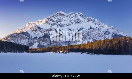 Congelati Lago di Johnson e distante la Cascade Mountain Scenic paesaggio invernale nel Parco Nazionale di Banff Canadian Rocky Mountains Foto Stock