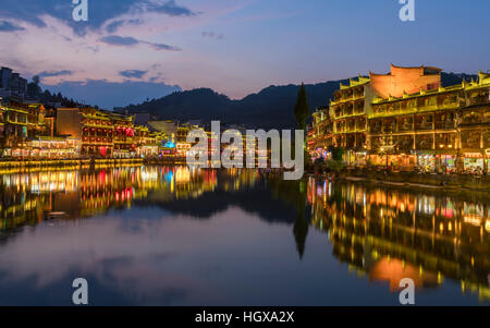 Luci accese gli edifici tradizionali di Fenghuang antica città dalla banca del tuo fiume castin riflessi colorati in acqua Foto Stock