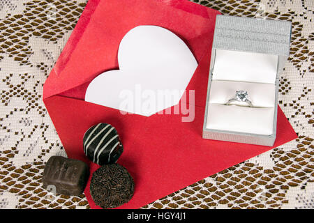 Scatola di cioccolatini e anello di diamante sulla busta rossa con cuore bianco Foto Stock