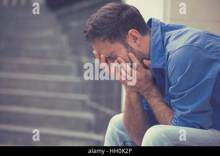 Profilo laterale ha sottolineato triste pianto giovane uomo seduto fuori tenendo la testa con le mani guardando verso il basso. Emozione umana sentimenti Foto Stock