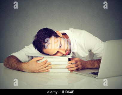 Troppo lavoro uomo stanco di dormire su libri al desk nella parte anteriore del computer. Pianificazione di occupato in un college, il lavoro, la privazione del sonno Foto Stock