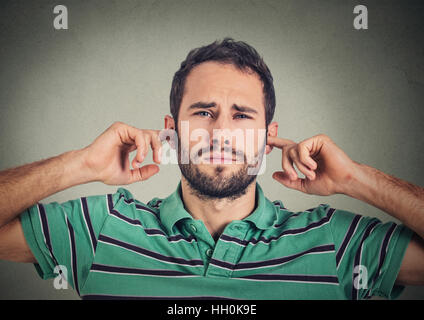 Headshot orinato uomo collegando le orecchie con le dita non vuole ascoltare isolato sul muro grigio sfondo Foto Stock