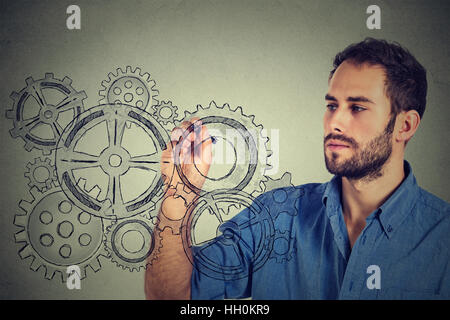Ingranaggi e idee il concetto di creatività. Giovane uomo ingranaggi di disegno con la penna sul muro grigio sfondo Foto Stock