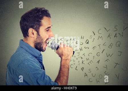 Giovane uomo a cantare in un microfono con alfabeto lettere provenienti dalla sua bocca. Comunicazione, informazione, concetto di intelligenza Foto Stock