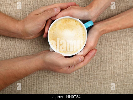 L uomo e la donna mani e abbracciando insieme grande piena tazza di cappuccino cappuccino caffè con latte schiumoso sopra tela di canapa tovaglia, close up, elevati t Foto Stock