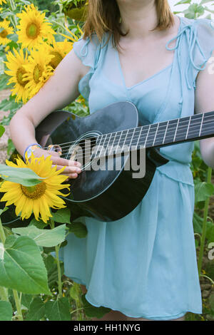 Giovane donna a suonare la chitarra in un campo di girasoli Foto Stock