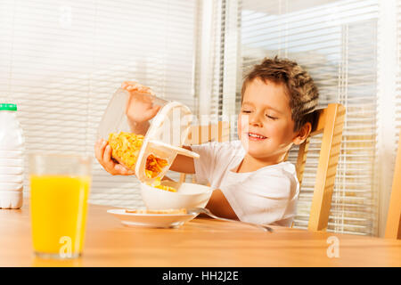 Little Boy versando corn flakes facendo colazione Foto Stock