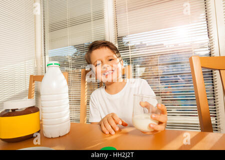 Felice ragazzo tenendo il vetro con il latte seduta a tavola Foto Stock