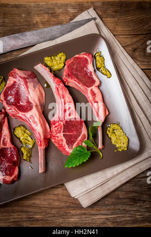 Crudo fresco costolette d'agnello con salsa su piastra su sfondo di legno, vista dall'alto Foto Stock